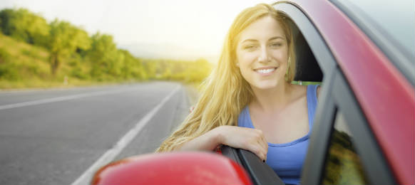 Beautiful young woman looking out of the car rental on a country road