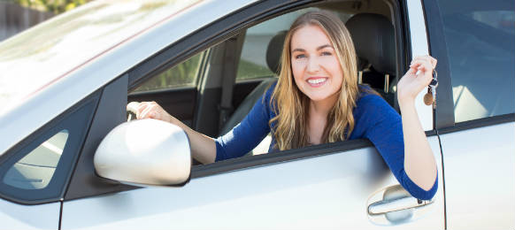 young woman sitting in her white car rental holding keys